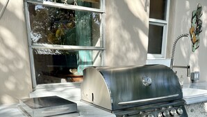 An outdoor kitchen with a stainless steel grill, a built-in oven, and a sink.