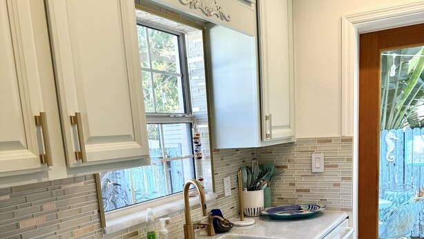 A kitchen with white cabinets, a built-in oven, a sink, and a window overlooking a backyard.