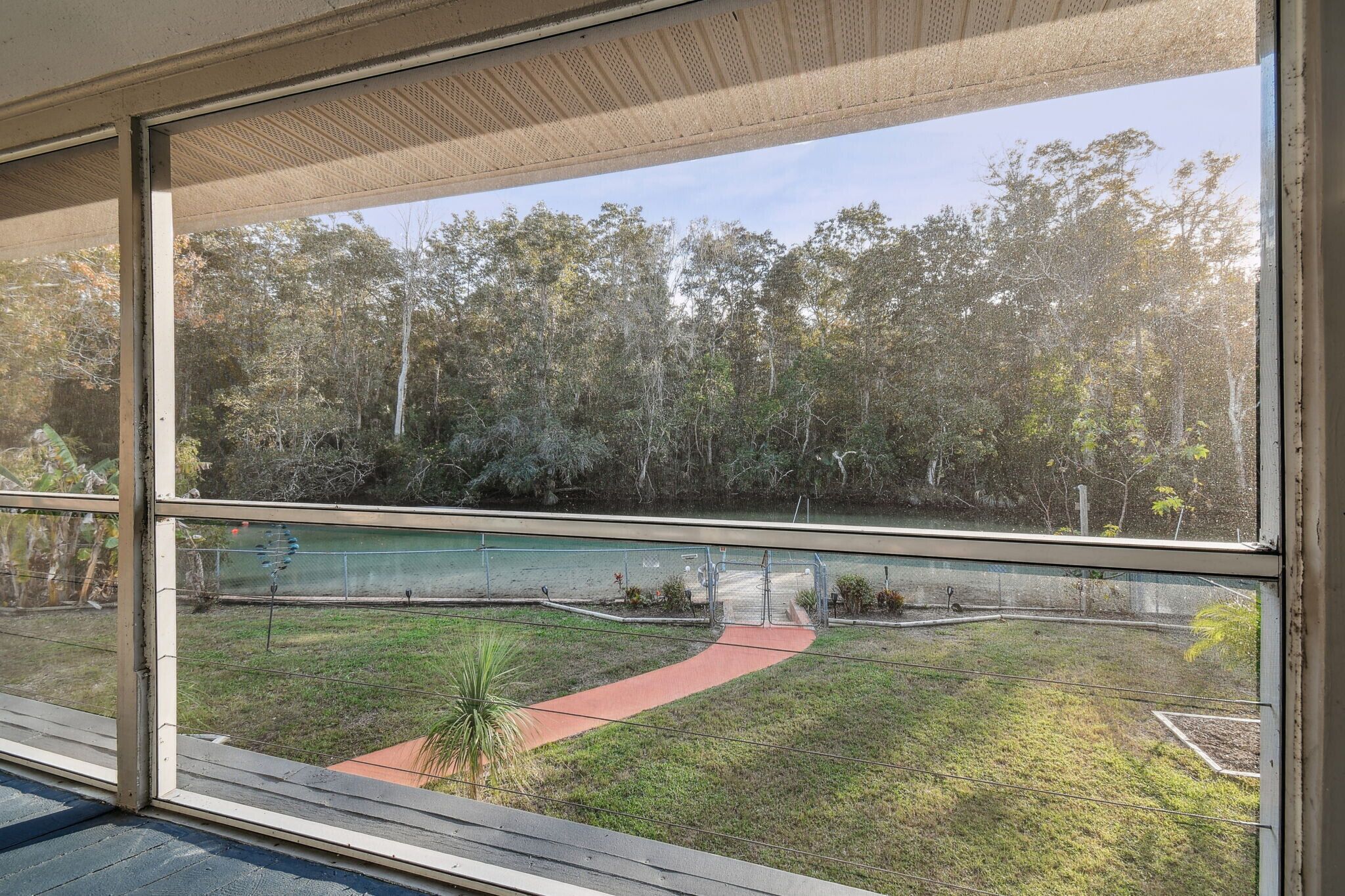 A view from a window overlooking a grassy area with a red path, trees, and a fence.