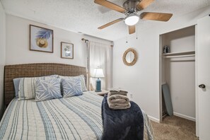 A bedroom with a bed, a ceiling fan, a nightstand with a lamp, a wall mirror, and a door leading to a closet. - Manatee Cove Apartment Star5vacations (Spring Hill)