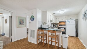 A modern kitchen with white cabinets, a microwave, and a refrigerator. There are two wooden chairs at a small table.