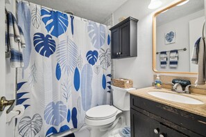 A bathroom with a shower curtain featuring a leaf pattern, a toilet, a sink with a makeup station, and a cabinet. - Manatee Cove Apartment Star5vacations (Spring Hill)