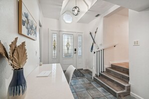 Un interior moderno con un mostrador de recepción blanco, un jarrón con hojas secas, una obra de arte enmarcada y una escalera con escalones de madera.
