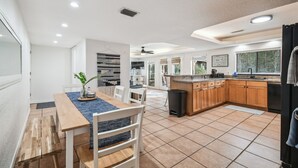 Una cuina moderna amb armaris de fusta, una zona de menjador amb taula i cadira, i una finestra gran que deixa entrar molta llum natural.