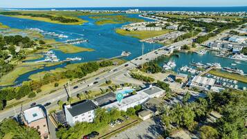 An aerial view of a marina with boats docked, a large building with a swimming pool, and surrounding greenery.