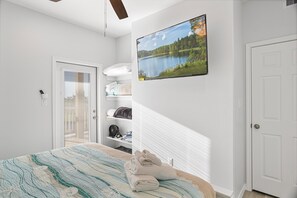 A bedroom with a bed, a wall-mounted TV, a door, and a window with blinds. - Beachfront, Heated Pool, 2 Hot Tubs, Lift, Putt Putt, Pet Friendly, Sleeps 32 (Bolivar Peninsula)