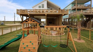 Een strandhuis met een houten terras, schommel en een zwembad.