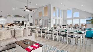 A spacious living area with a high ceiling, a dining table set for six, and a kitchen with modern appliances. - Beachfront, Heated Pool, 2 Hot Tubs, Lift, Putt Putt, Pet Friendly, Sleeps 32 (Bolivar Peninsula)