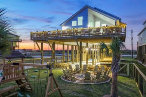 A two-story house with a covered patio area, outdoor seating, and a swing set. - Beachfront, Heated Pool, 2 Hot Tubs, Lift, Putt Putt, Pet Friendly, Sleeps 32 (Bolivar Peninsula)