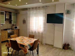 Cocina compacta con comedor, televisor montado en la pared y planta en una estantería.