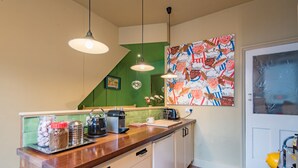 Een keuken met een houten aanrecht, hangende hanglampen, een groene achterwand en een wanddecoratie.
