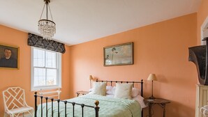 Een slaapkamer met een bed, een stoel, een raam en een schilderij aan de muur.