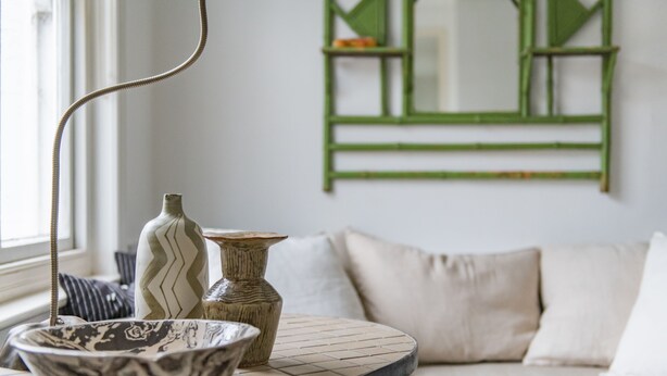 Een kamer met een ronde tafel, twee vazen en een spiegel met groene lijst.