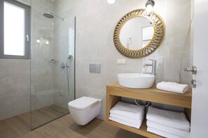 Et moderne badeværelse med et glasbadeværelsesafskærmning, et hvidt toilet, en trækommode med en hvid vask og et dekorativt spejl.