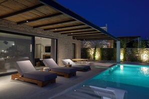 Relax by the clear pool surrounded by lounge chairs and a shaded area under a pergola.