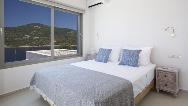 Une chambre avec une grande fenêtre, un lit avec une literie à motifs, des tables de chevet et une vue sur une colline.