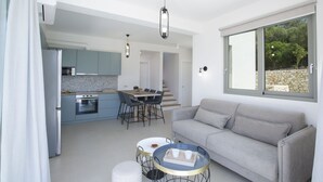 Una cocina moderna con comedor, un sofá gris y un ventanal con vistas a árboles.