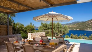 Un área de comedor al aire libre con una mesa dispuesta para el desayuno, con vista a una piscina y al mar.