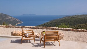 Una terrazza con due sedie di legno e un tavolo, affacciata su un pittoresco paesaggio costiero.