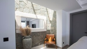 Un bagno moderno con una parete in pietra, un ampio specchio, una sedia di legno e un vaso grande con piante secche.