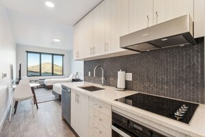 A modern kitchen with a large window, a built-in stove, and a herringbone-patterned backsplash.