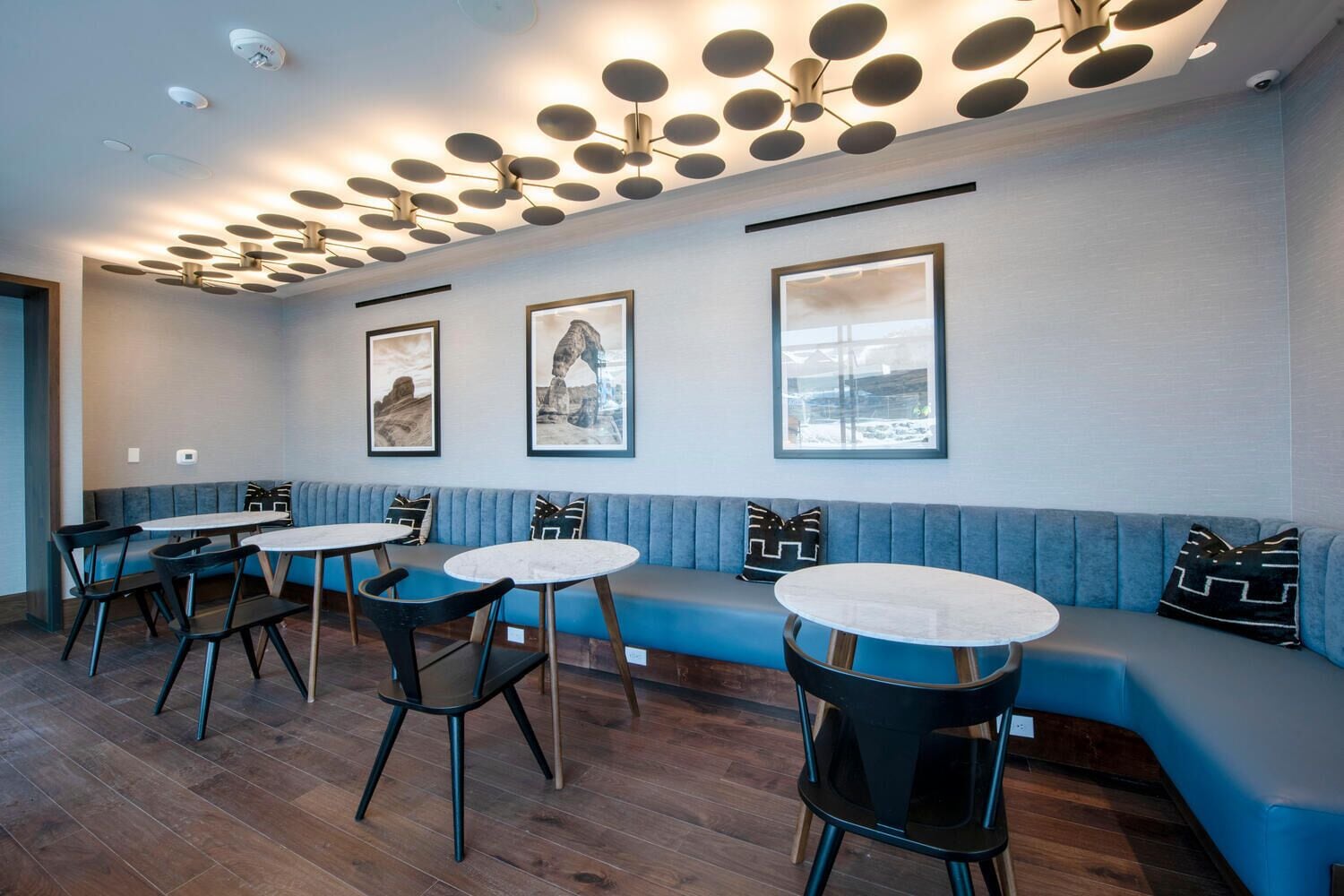 A modern interior with a blue cushioned bench, round tables, and black chairs.