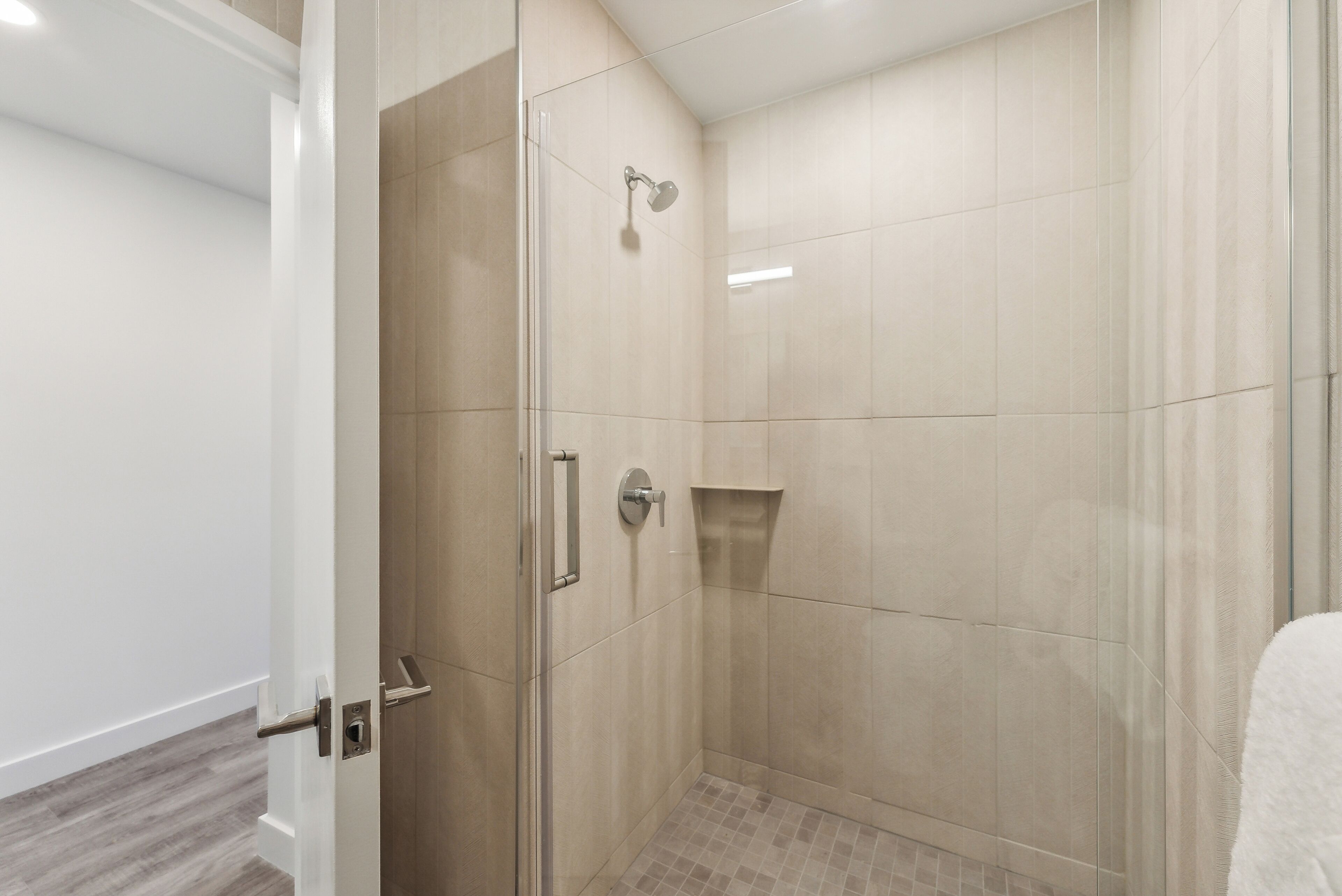 Una ducha moderna con puerta de vidrio, cabezal de ducha de mano y un estante pequeño.