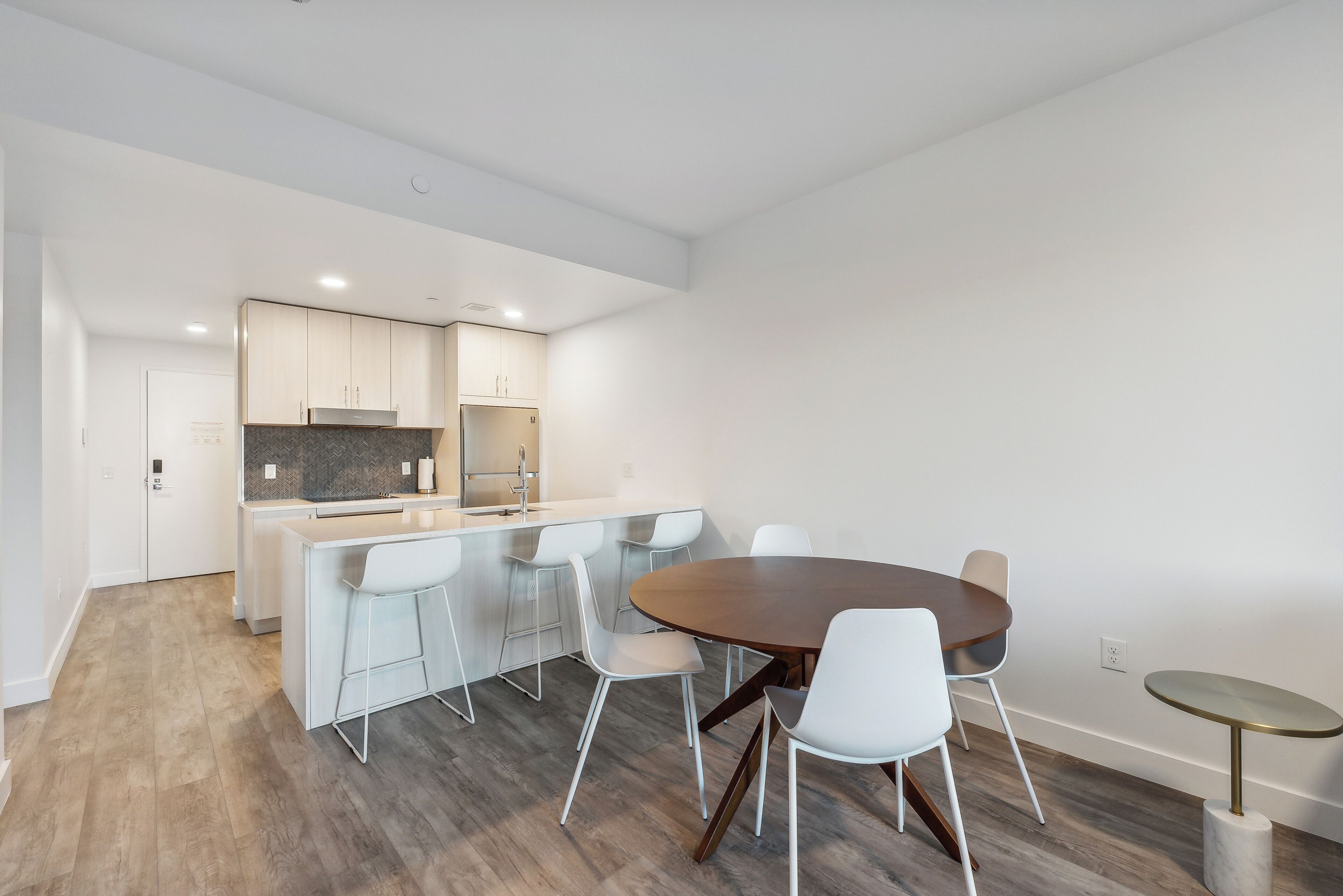 A modern kitchen with white cabinets, a central island, and a dining area with a round table and chairs.