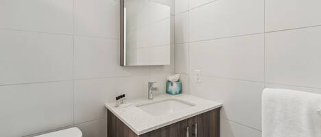 A modern bathroom with a white toilet, a sink with a mirror above it, and a towel hanging on the wall.