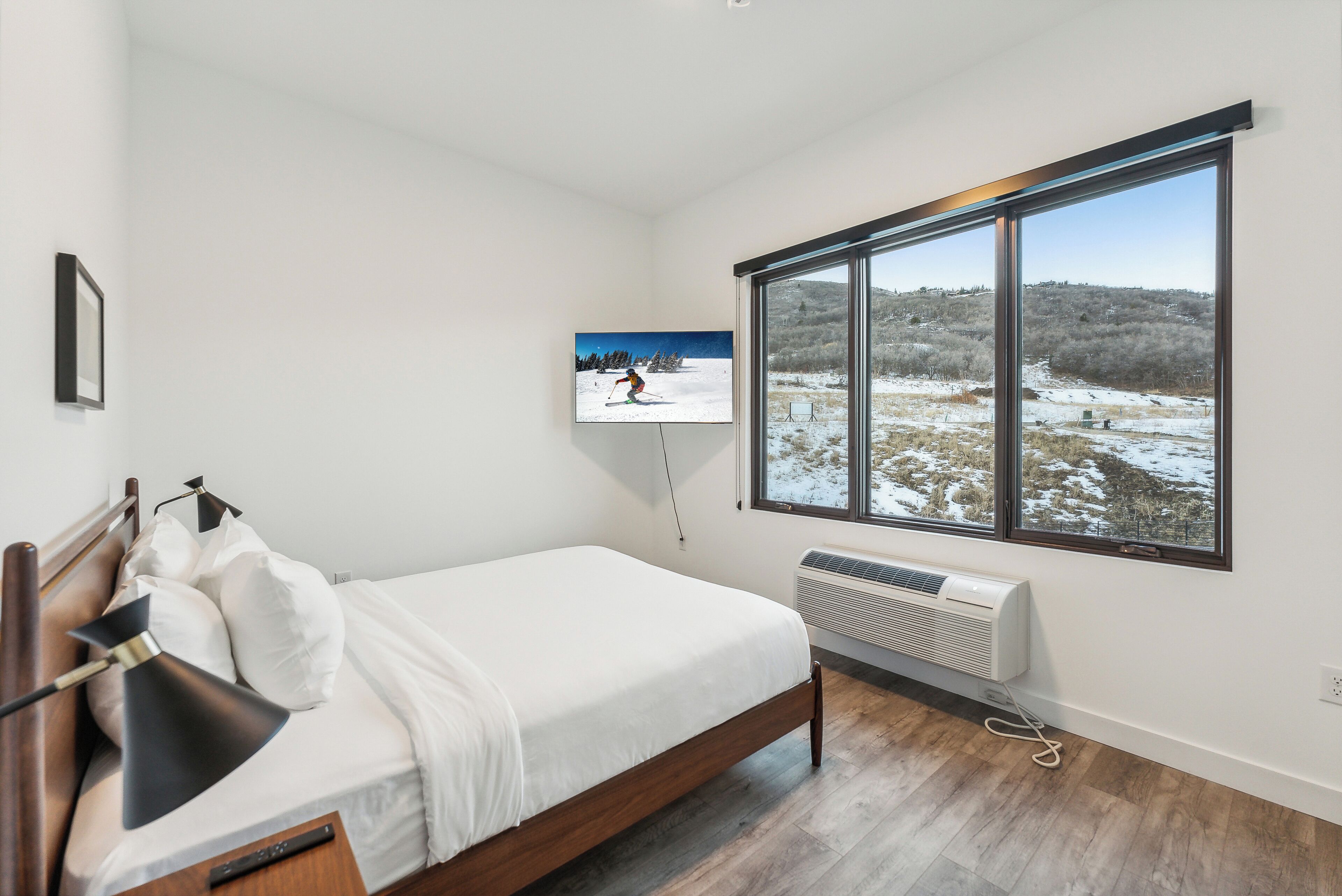 Une chambre moderne dotée d’une grande fenêtre, d’un lit, d’une télévision et d’un climatiseur fixé au mur.