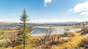 A mountainous landscape with a lake, a snow-covered hill, and sparse vegetation.