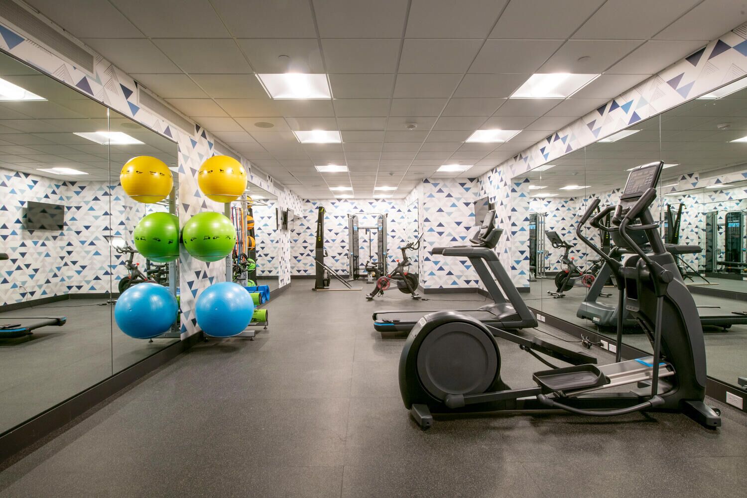 Un gimnasio con equipo de ejercicio, espejos y paredes con diseño.