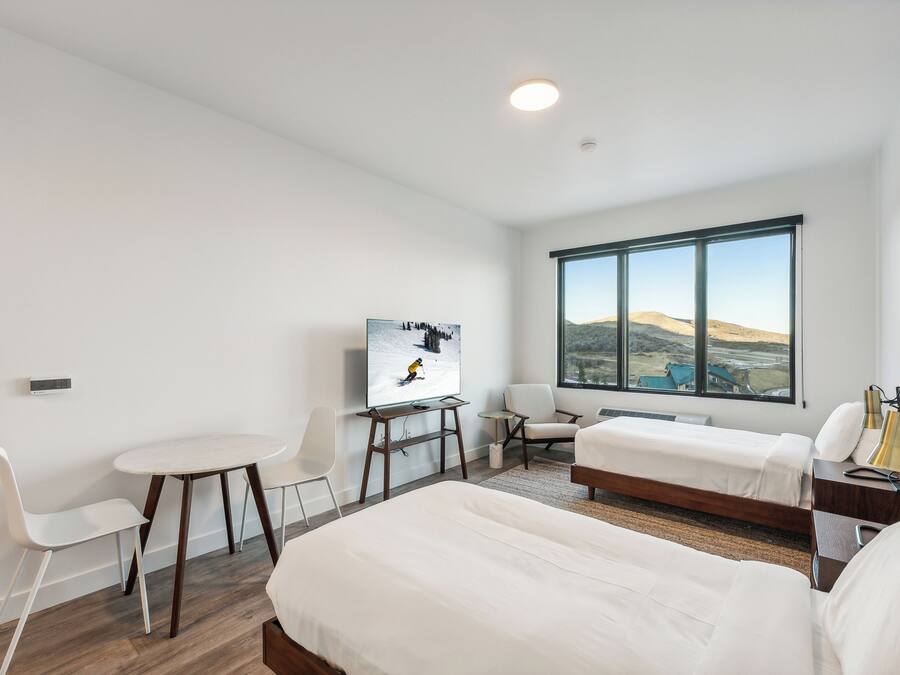 Ein modernes Hotelzimmer mit zwei Betten, einem Fernseher, einem Schreibtisch und einem großen Fenster mit schöner Aussicht.