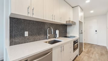 A modern kitchen with a herringbone-patterned backsplash, stainless steel appliances, and light wood cabinetry.