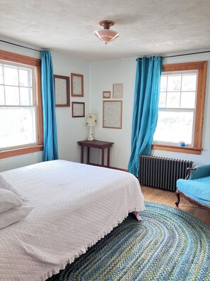 A bedroom with a bed, a radiator, a lamp, and framed pictures on the wall.