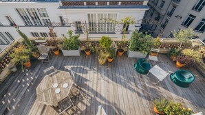 A rooftop terrace with wooden flooring, potted plants, outdoor furniture, and a view of surrounding buildings. - 2 storey luxury penthouse with large terrace but no elevator (Paris)
