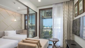 A modern hotel room with two beds, a sofa, a small table, a TV, and a balcony with a view. - The Proud Karon Beach Phuket Trademark Collection By Wyndham (Karon)