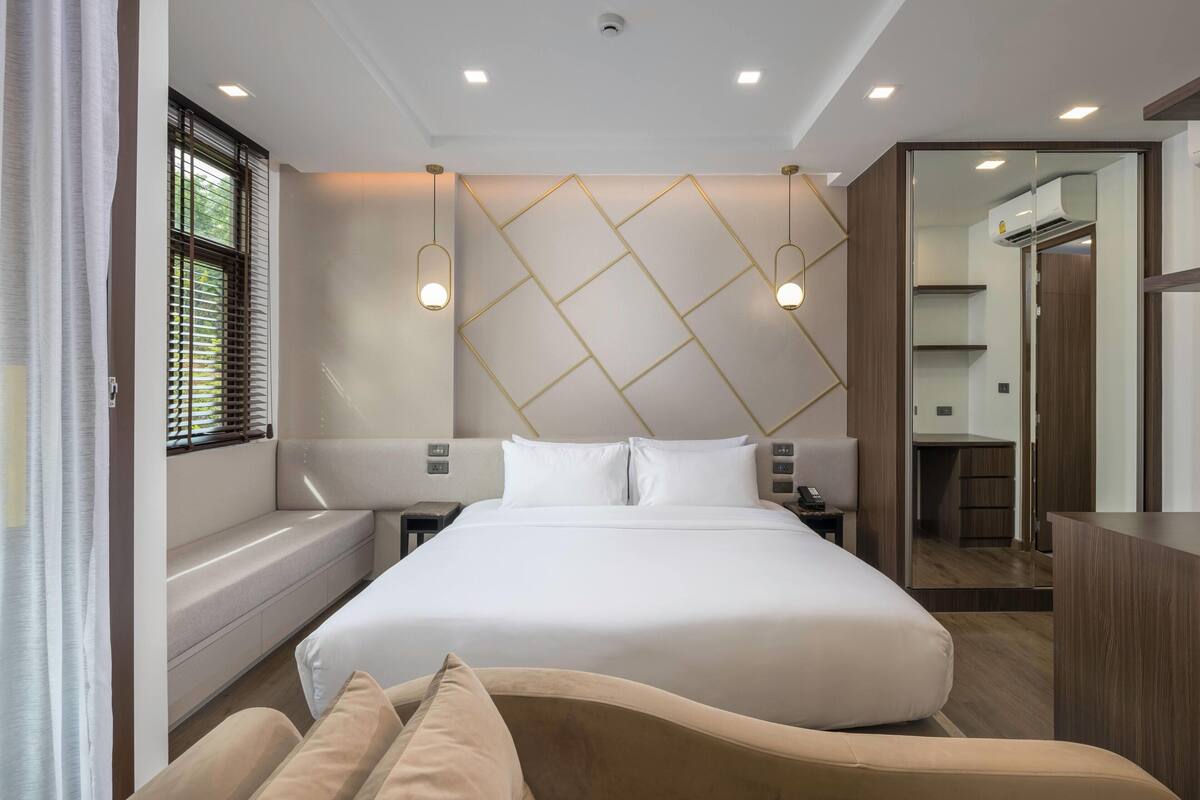 Une chambre d’hôtel moderne avec un grand lit, des tables de chevet, une banquette intégrée et un miroir.