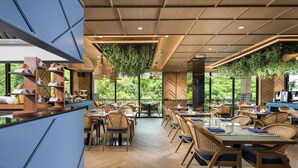 A restaurant with wooden tables and chairs, hanging plants, and a view of greenery outside. - The Proud Karon Beach Phuket Trademark Collection By Wyndham (Karon)