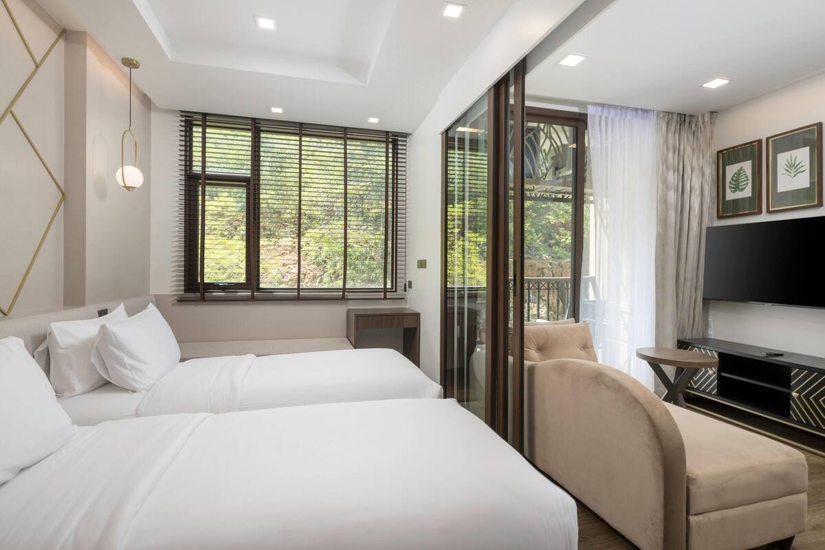 Une chambre d’hôtel avec deux lits, une télévision, un balcon donnant sur la verdure et une porte-fenêtre coulissante.