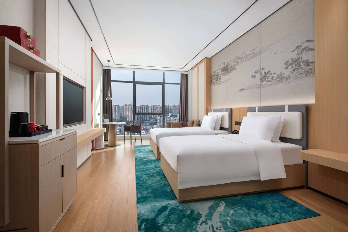 Une chambre d’hôtel moderne, dotée de deux lits, d’un bureau, d’une télévision et d’une grande fenêtre donnant sur la ville.