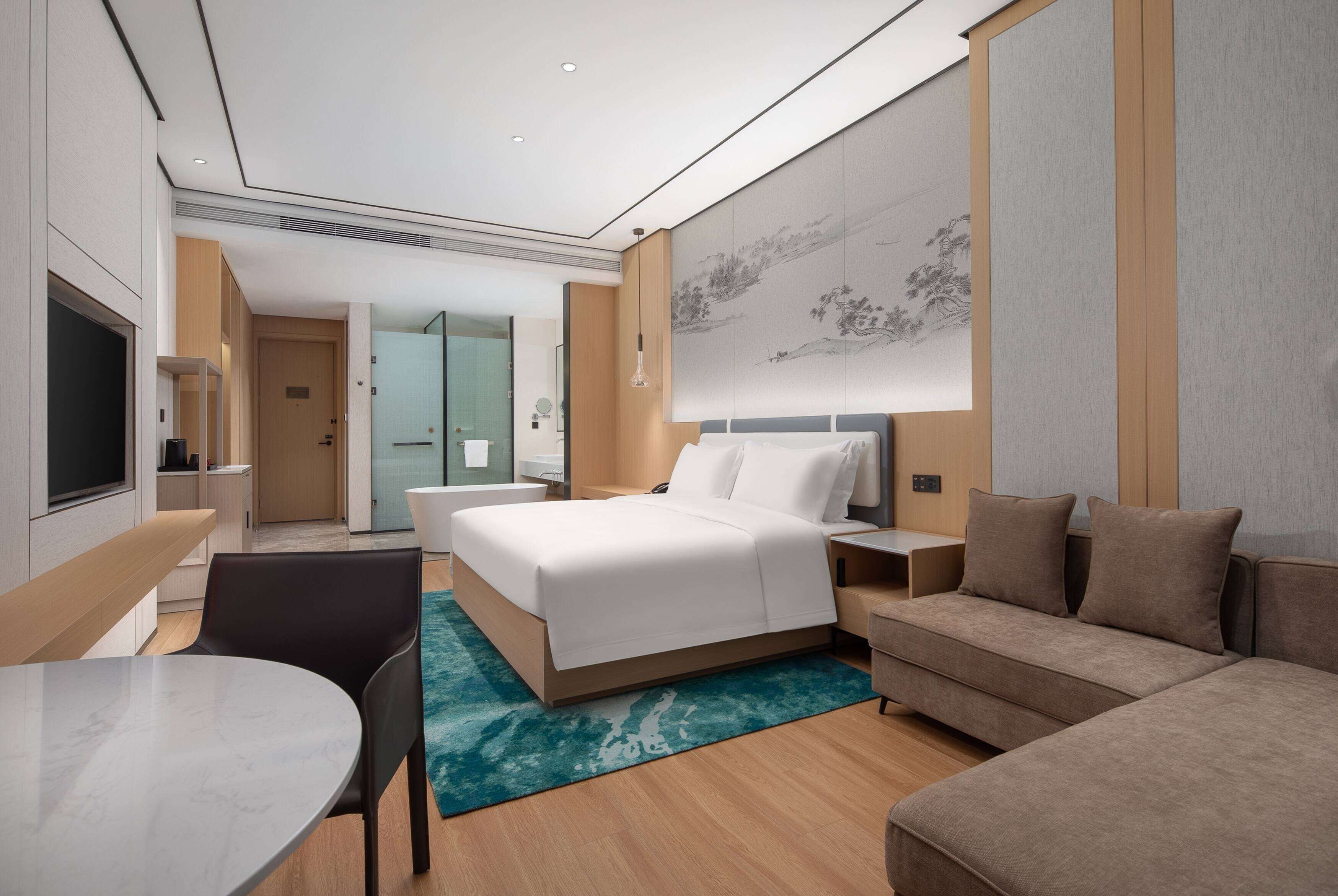 A modern hotel room with a bed, a sofa, a desk, and a TV.