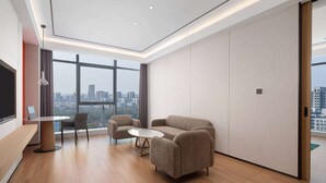 A modern hotel room with a large window, a sofa, a small round table, and a TV.