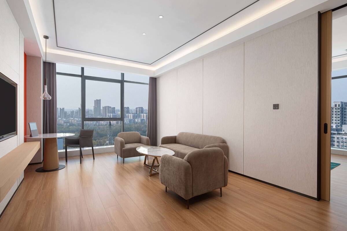 Une chambre d’hôtel moderne avec une grande fenêtre, un canapé, une petite table ronde et un téléviseur.