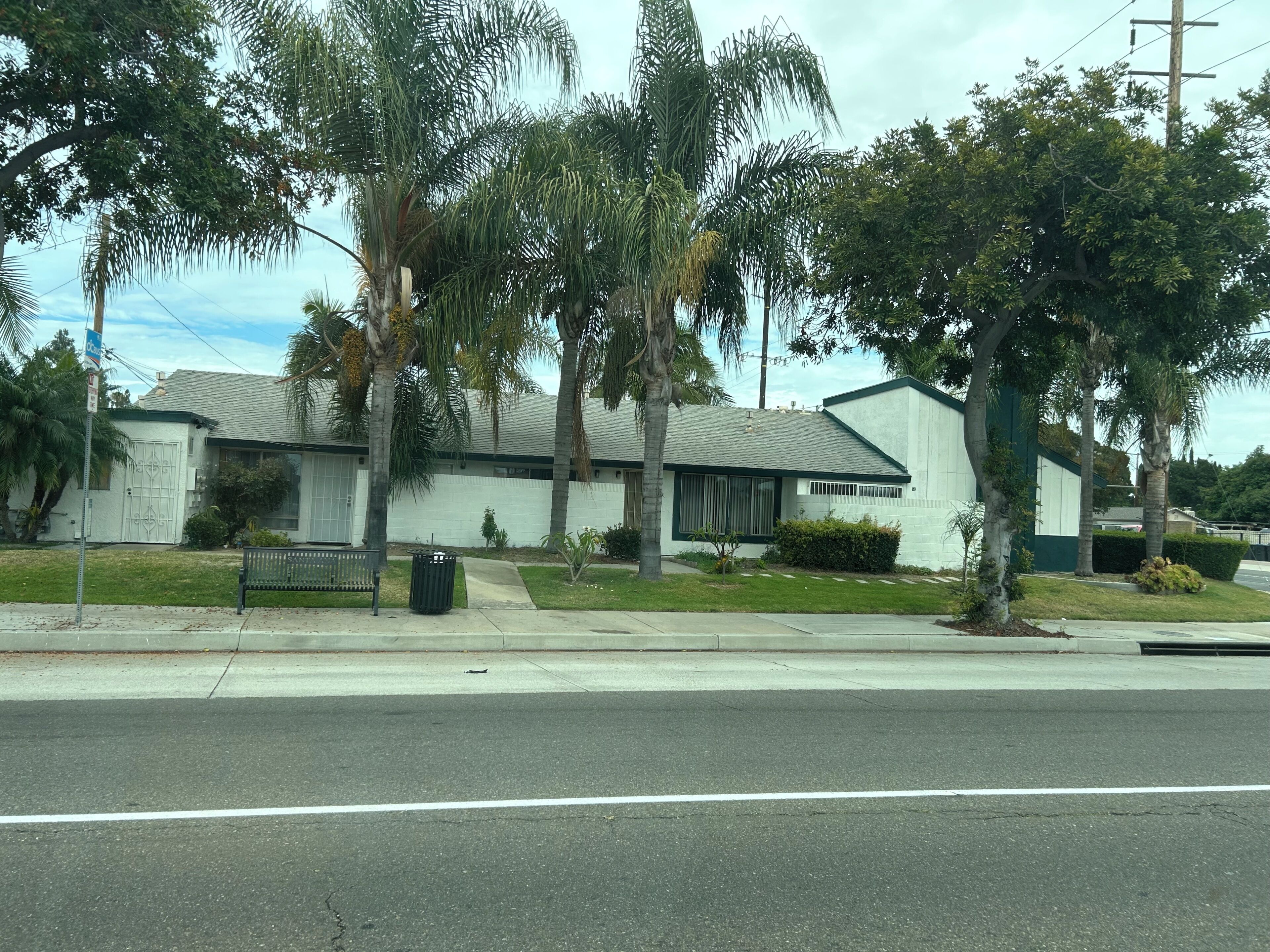 A residential house with a garage, a front yard with a bench, and a street view.