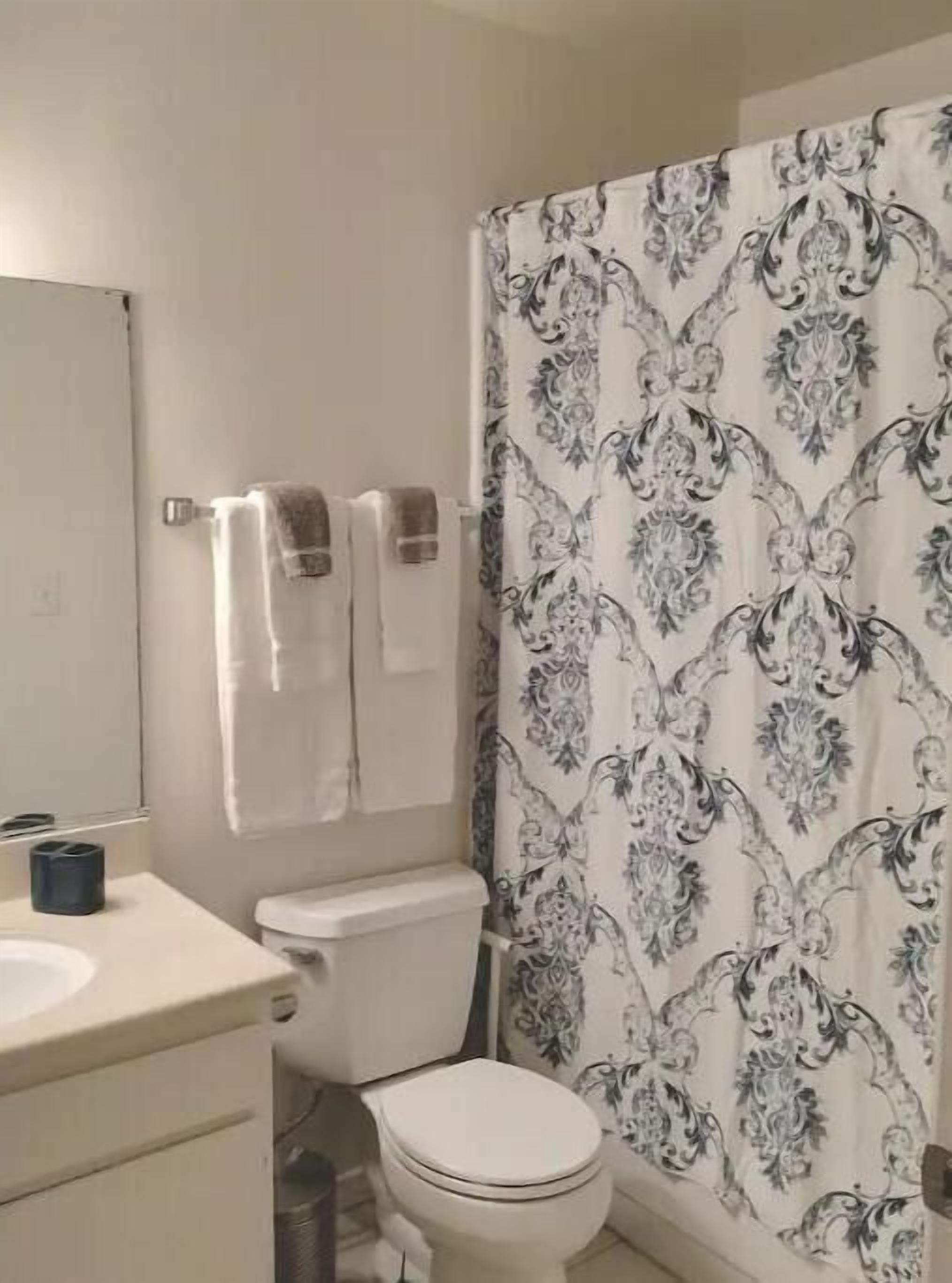 Une salle de bain équipée de toilettes, d’un lavabo et d’un rideau de douche à motifs floraux.