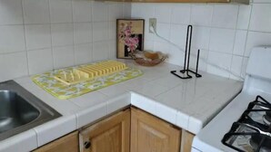 Une cuisine avec des meubles de rangement en bois, un évier, une cuisinière à gaz et une planche à découper jaune posée sur le plan de travail.