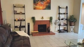 Un salon avec une cheminée, un canapé, une table basse en verre et deux étagères remplies d’objets décoratifs.