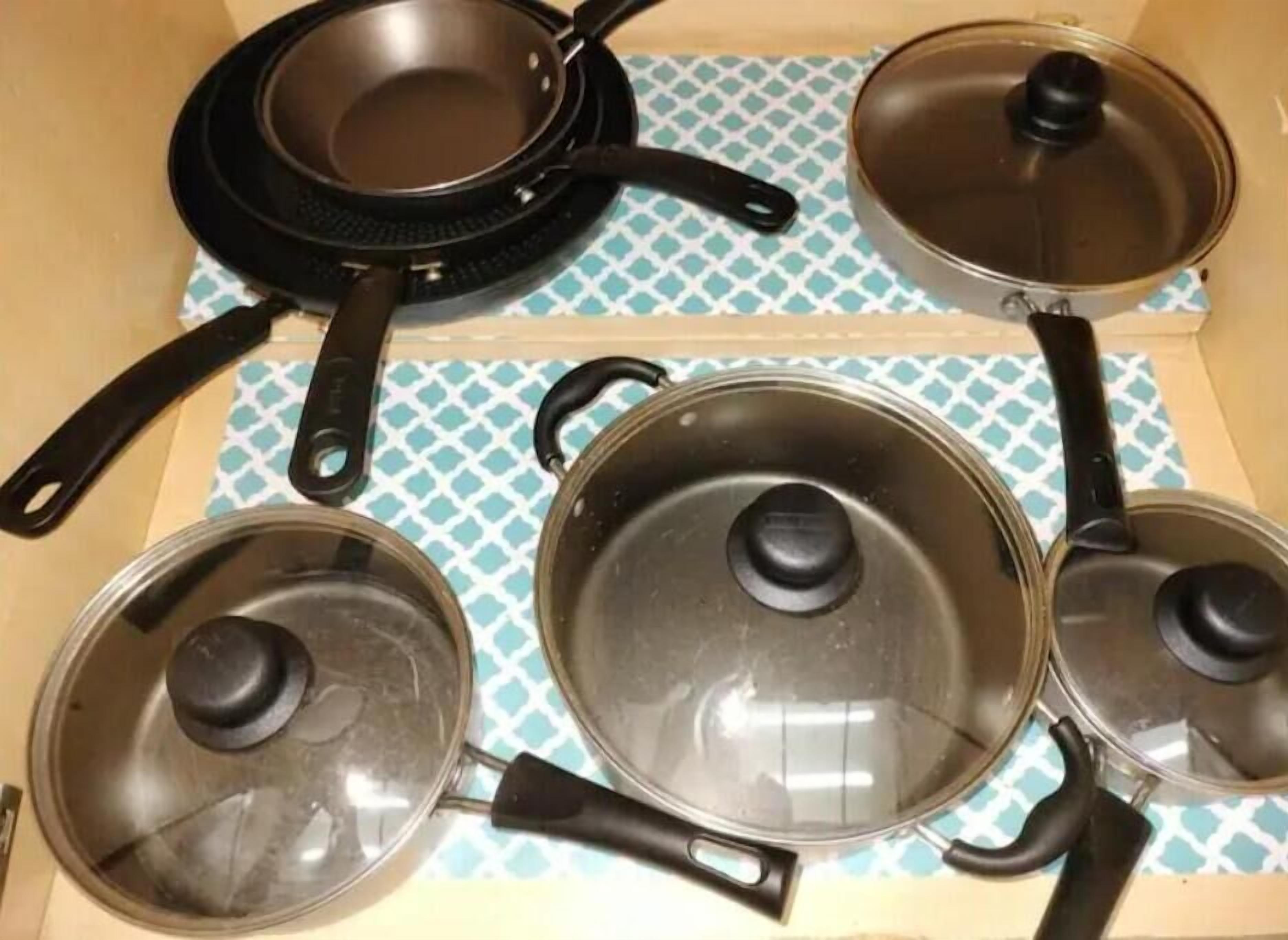 A kitchen drawer with four frying pans and two lids.