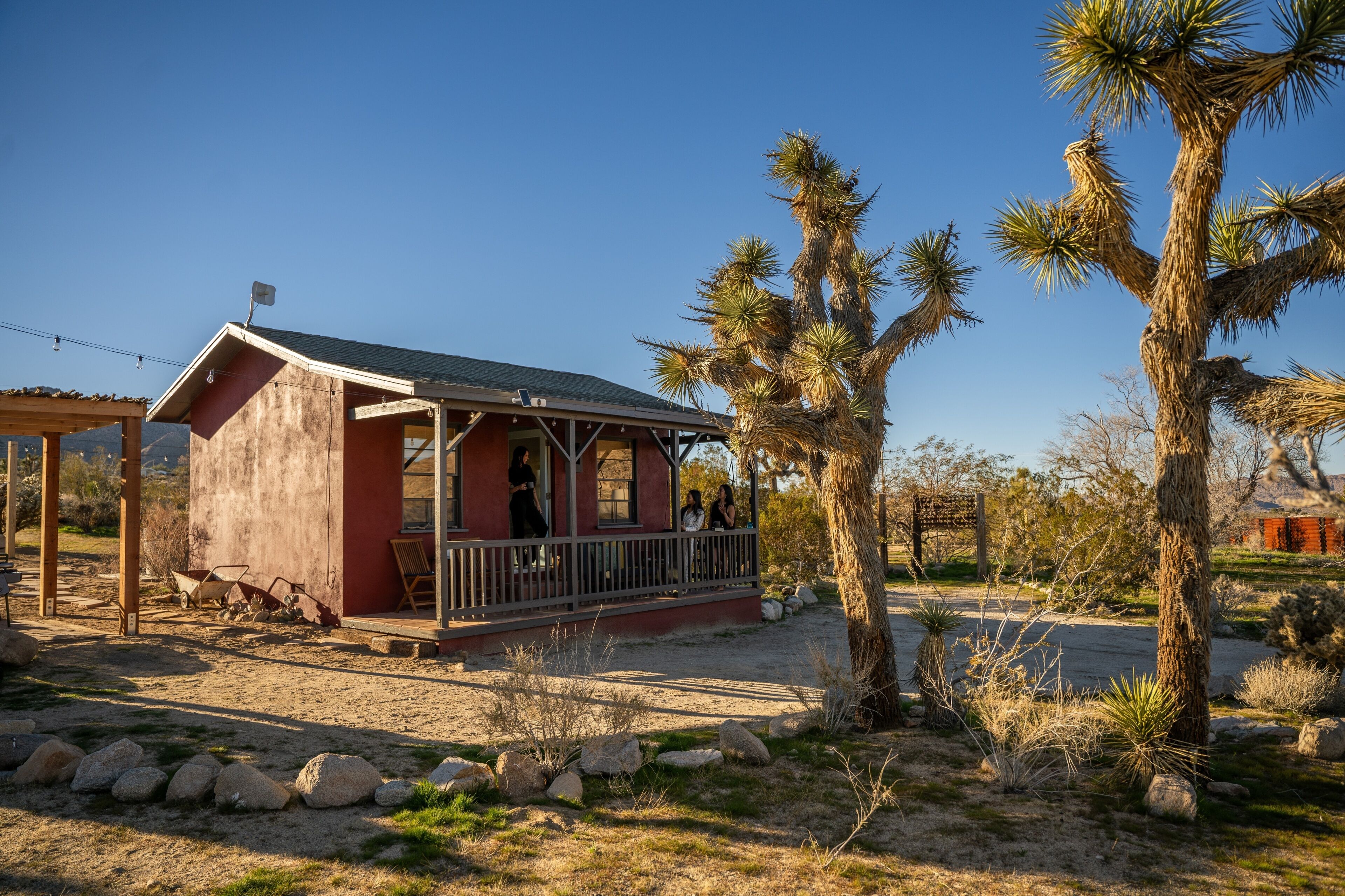 A small red building with a porch, surrounded by desert vegetation and a clear sky.